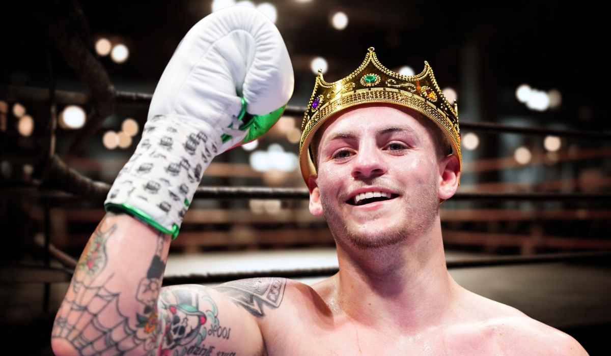 A smiling boxer wearing a crown and raising a gloved fist in the ring
