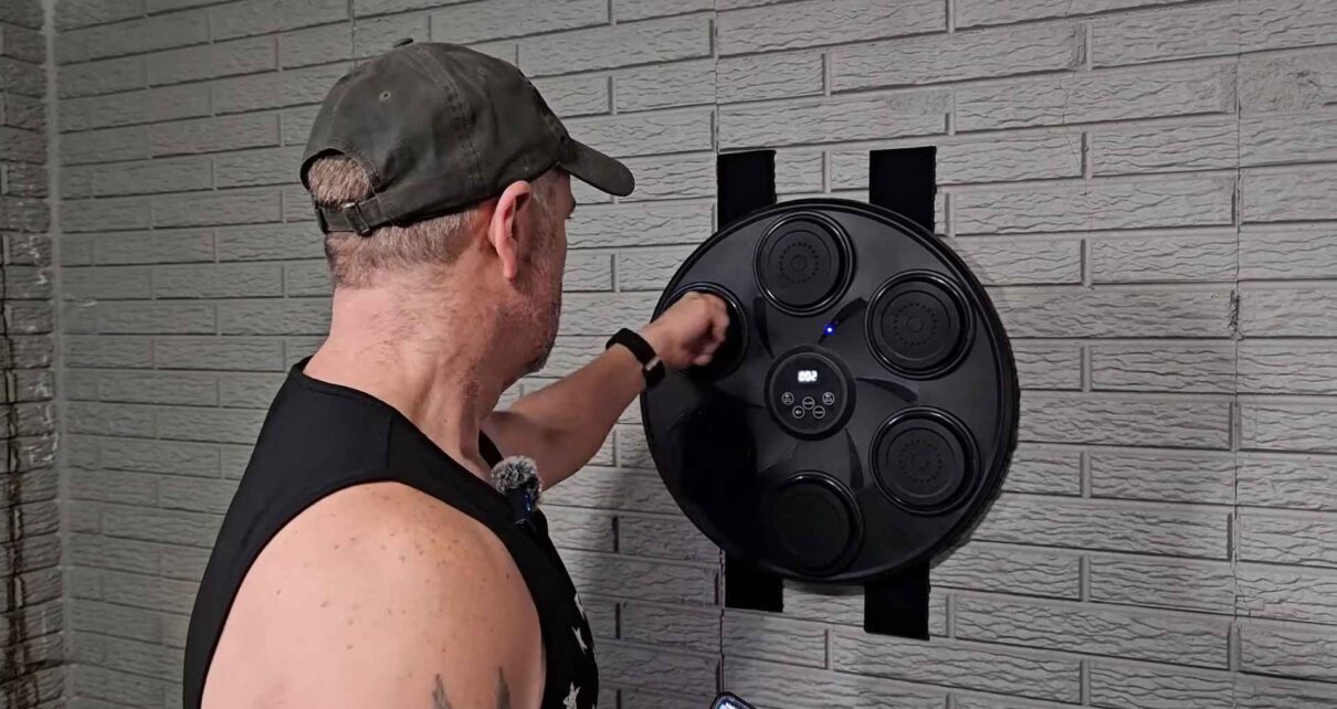 Man punching an electronic boxing pad mounted on a brick wall