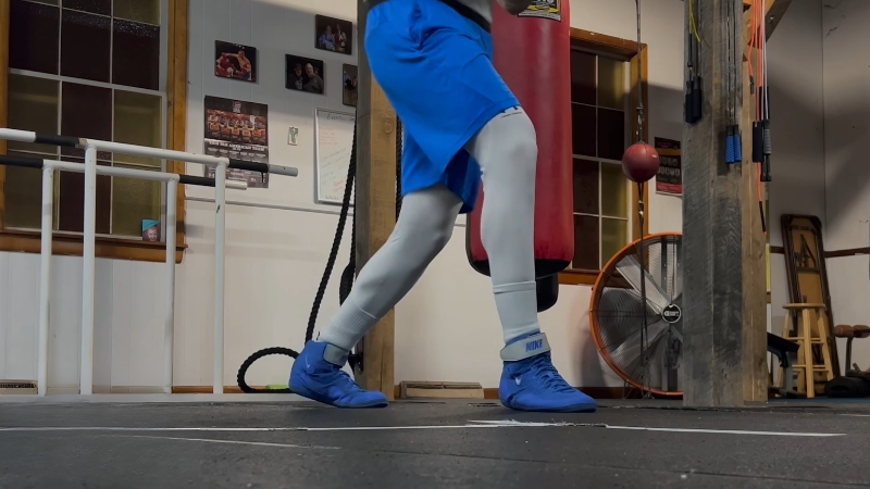 Boxer steps through a square pattern on the floor to practice controlled footwork in a gym