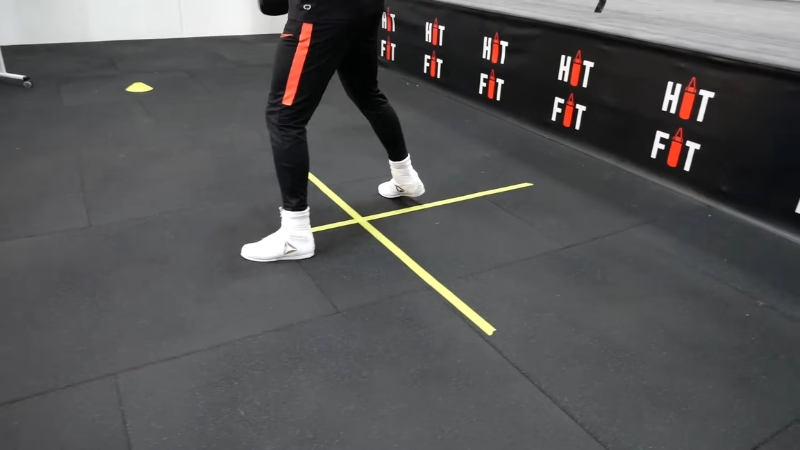 Boxer steps across taped lines on the floor to practice controlled footwork movement