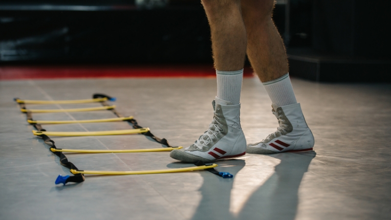 Boxing footwork drills with an agility ladder as a beginner practices quick, controlled steps on a gym floor