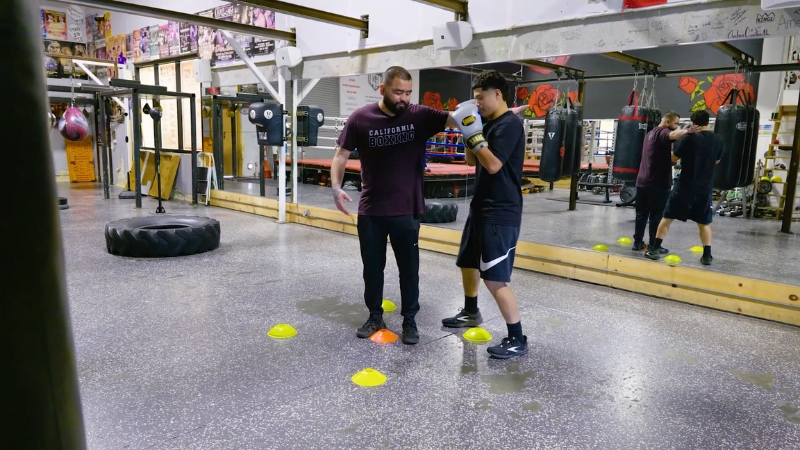 Boxer moves between cones as a coach gives direction cues during a footwork drill