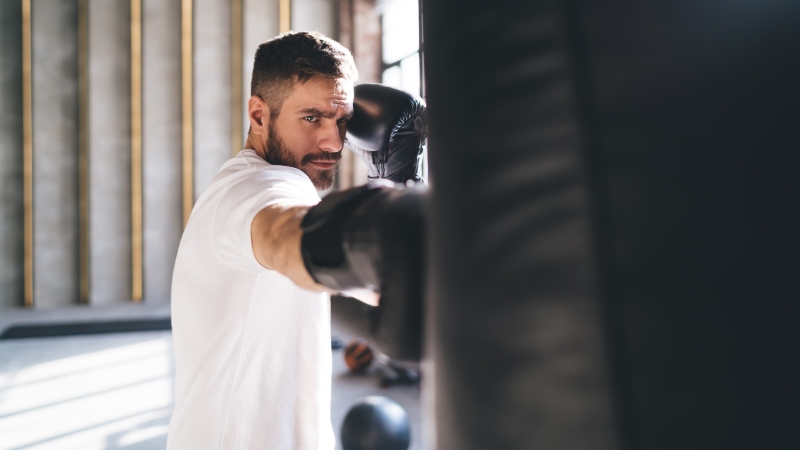 Man throws a straight punch at a heavy bag while staying balanced in a boxing stance