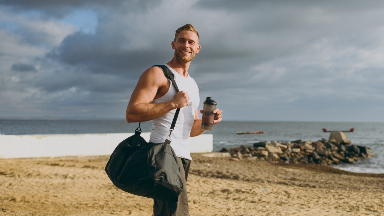Man with gym bag holding a protein shake before a boxing workout near the beach