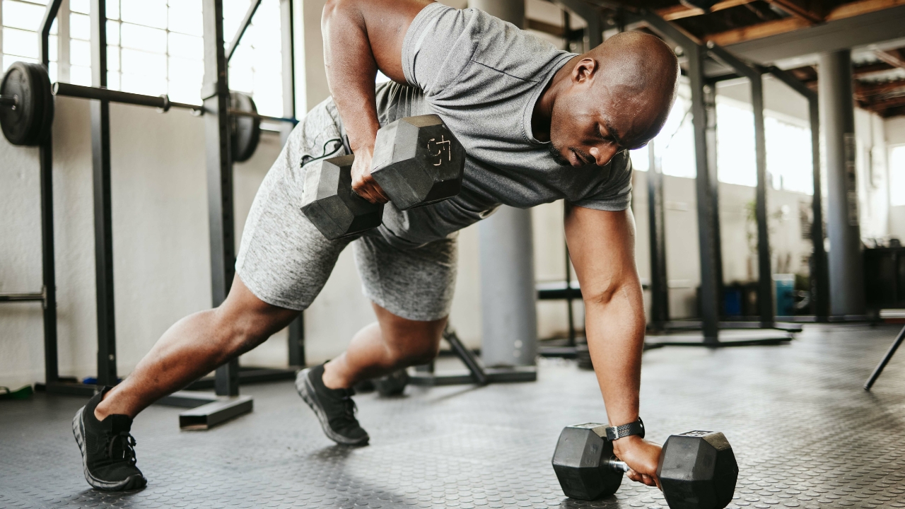 Man performs one-arm dumbbell row on gym floor